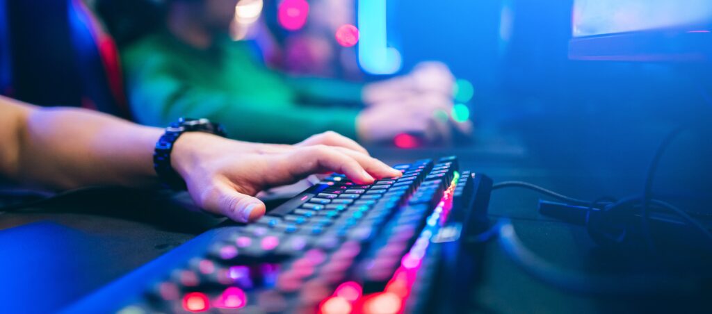 Mano de gamer utilizando teclado mecánico con retroiluminación RGB durante partida en PC.