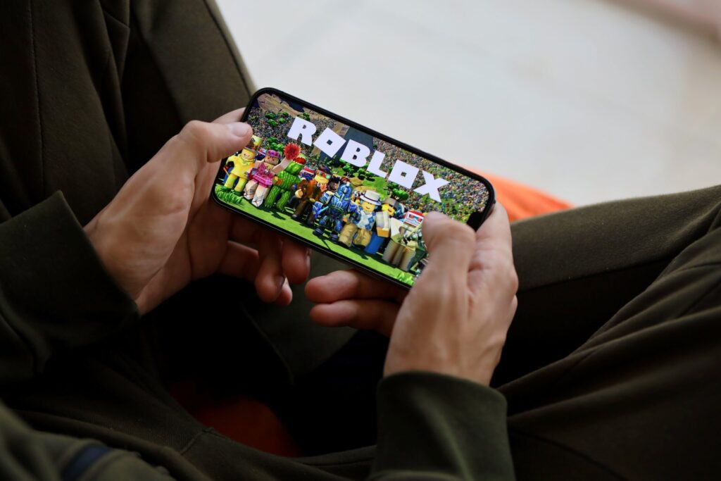 Persona juega Roblox en un teléfono móvil mostrando personajes y logotipo, ilustrando la demanda en Luisiana por seguridad infantil en la plataforma de videojuegos.