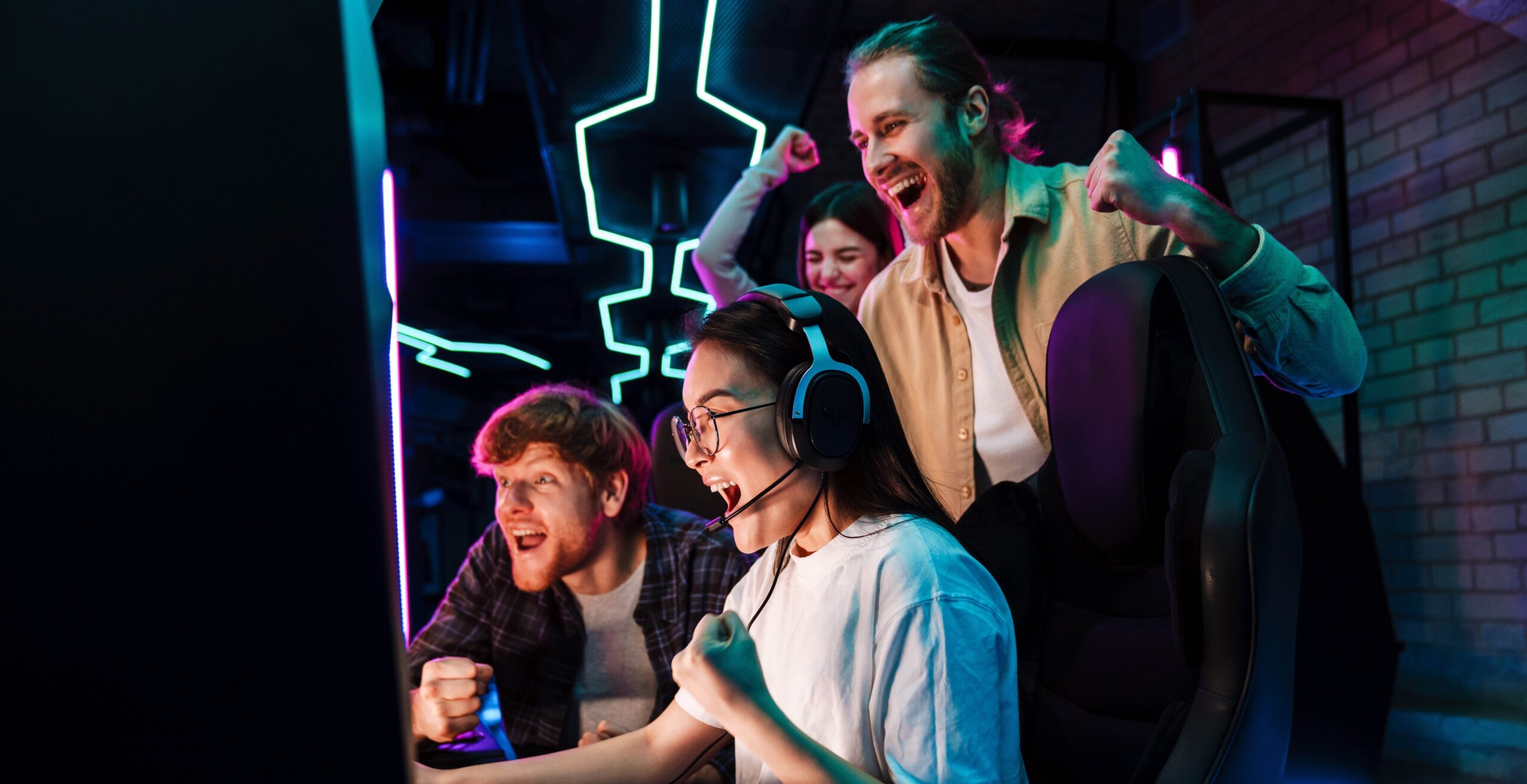 Grupo de jóvenes gamers celebrando una victoria frente a la pantalla en un ambiente con luces de neón.