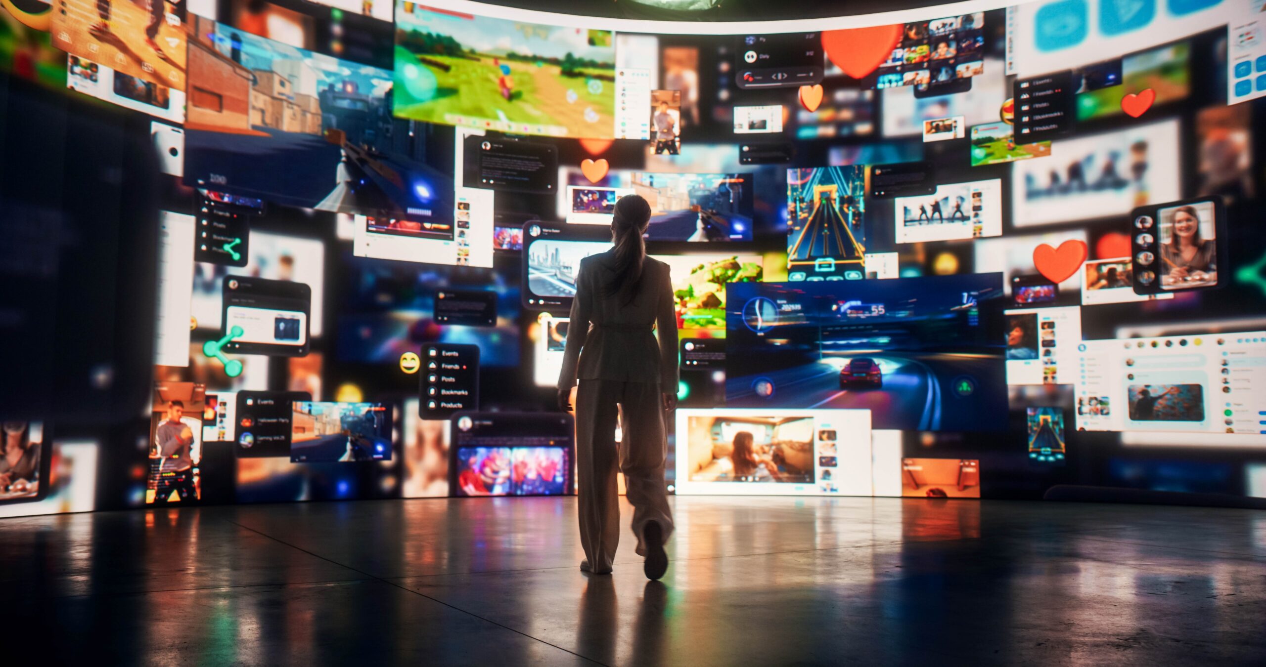 Persona de espaldas observando una gran pantalla curva llena de imágenes de videojuegos, transmisiones en vivo y redes sociales, con íconos de corazones y reacciones.