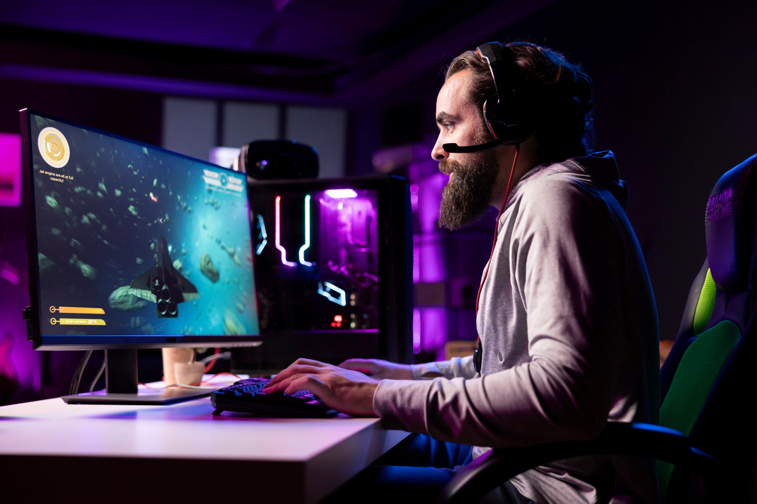 Hombre joven con auriculares juega en computadora de escritorio en un entorno gamer con luces de neón, representando la fuerza de la industria de videojuegos en Reino Unido.