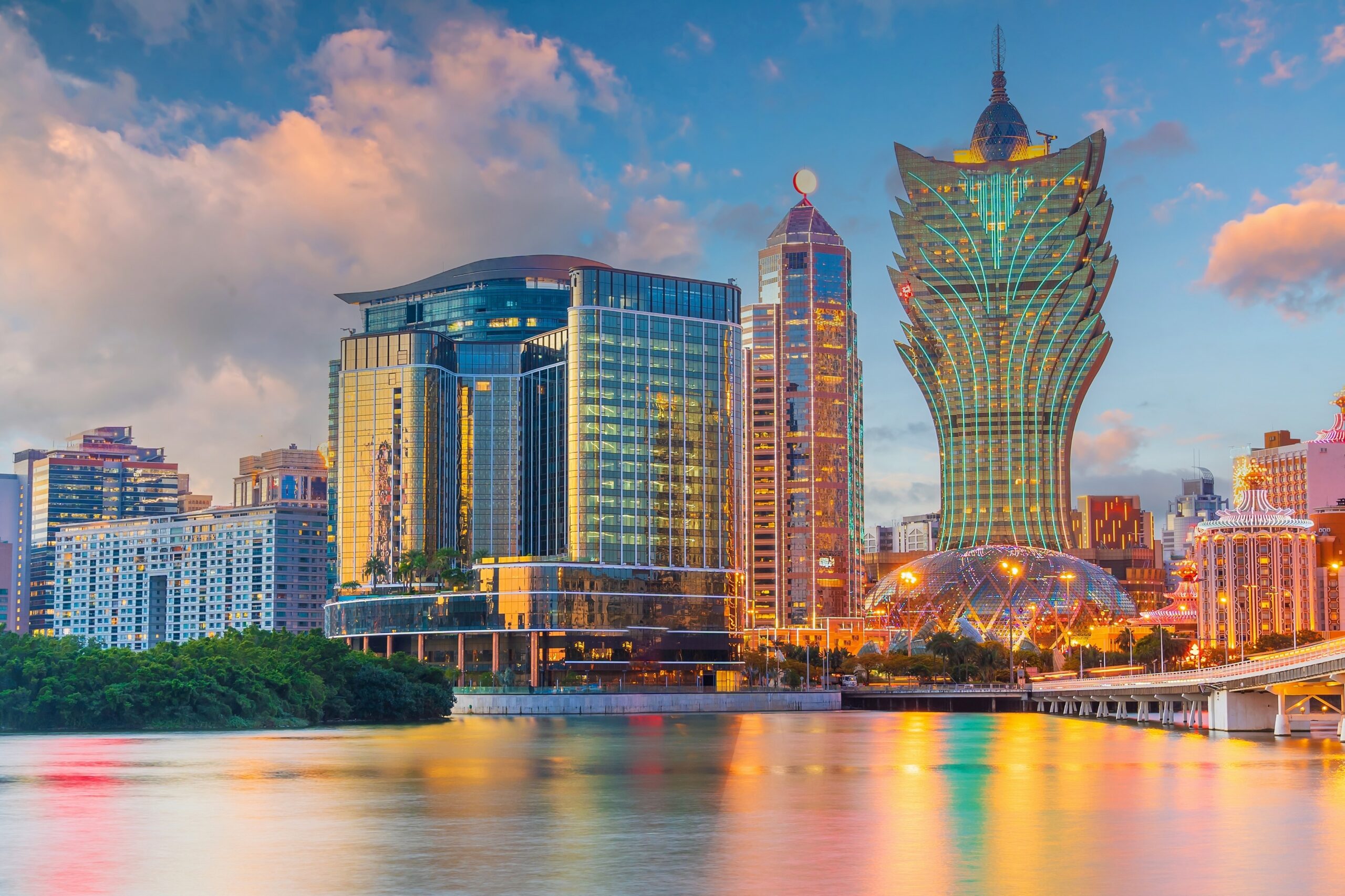Vista panorámica de los casinos y rascacielos de Macao iluminados al atardecer, reflejados sobre el agua.