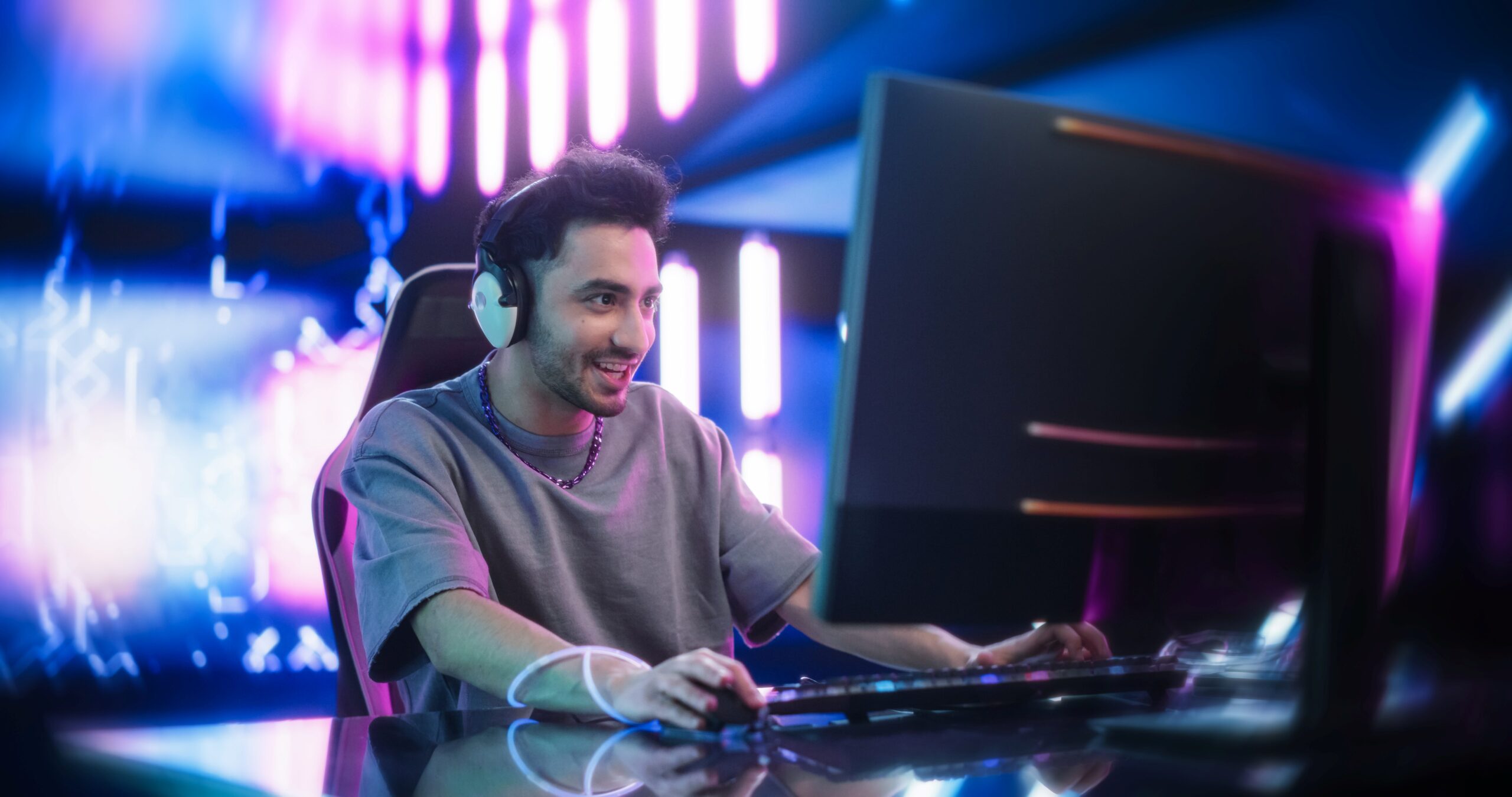 Hombre joven juega en PC con auriculares en ambiente gamer futurista, reflejando la emoción por Black Myth Zhong Kui en consolas y computadora.