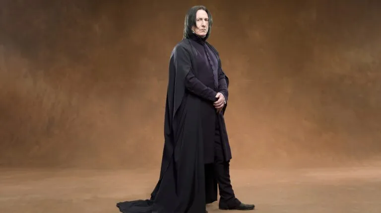 Alan Rickman caracterizado como Severus Snape, de cuerpo completo, con su larga capa negra y traje abotonado.